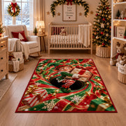A smiling elf clutches a wrapped present while sitting inside a red and green spiral; rug shown in a festive nursery
