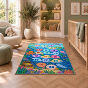 Blue ocean hopscotch rug with numbered bubbles, coral, fish and sea animals, shown in a bedroom setting