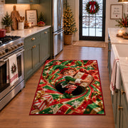 A smiling elf clutches a wrapped present while sitting inside a red and green spiral; rug shown in a holiday kitchen