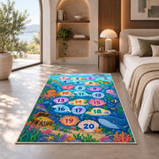 Blue ocean hopscotch rug with numbered bubbles, coral, fish and sea animals, placed on a wood floor near furniture