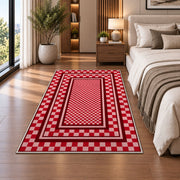 Red and Pink Checkered Border area rug in a bedroom beside the bed