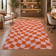 Wavy Orange and Pink Checkerboard area rug in a study with an armchair and bookshelves