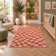 Wavy Orange and Pink Checkerboard area rug in a nursery with a crib and armchair