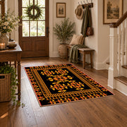 Black and orange tribal area rug with bold geometric border motifs, wood floor styling
