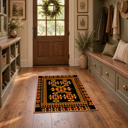 Black and orange tribal area rug with bold geometric border motifs, front room mockup